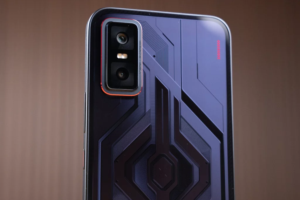 A vertical, close-up shot of the black Infinix GT 30 Pro, focusing on the back of the phone. The image shows the intricate, dark geometric patterns and the rectangular camera module with a red outline.
