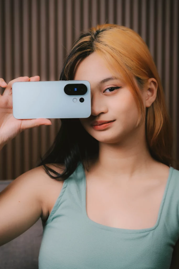 Woman holding a light-colored smartphone horizontally, partially covering her face.