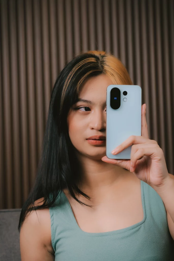 Woman with two-toned hair holding a light-colored smartphone vertically, covering part of her face.
