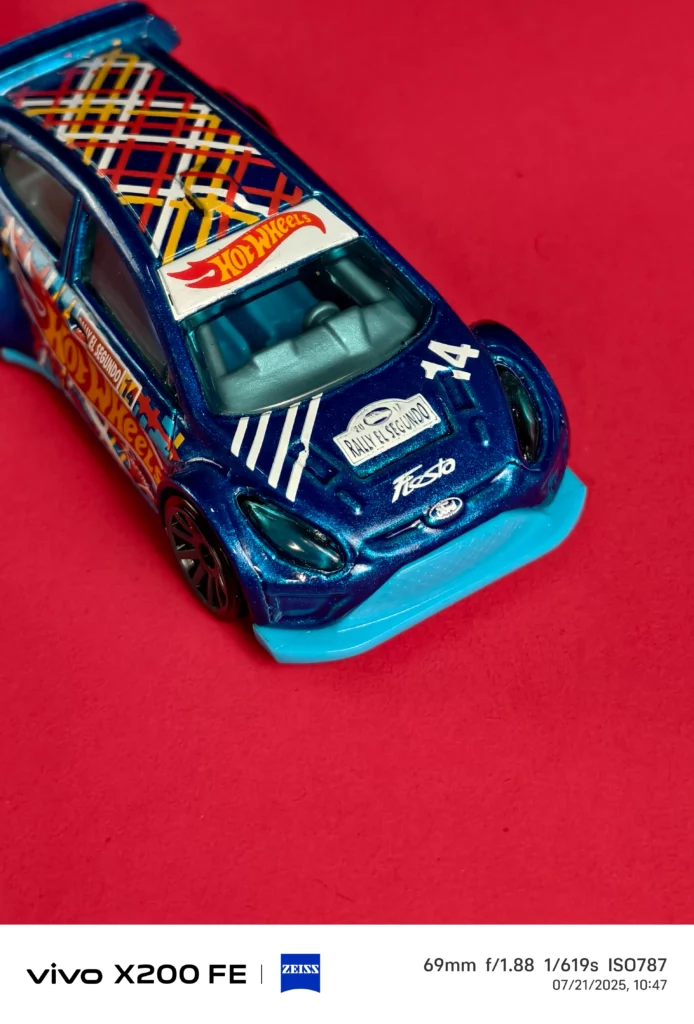 Close-up of a blue Hot Wheels rally car on a red background.