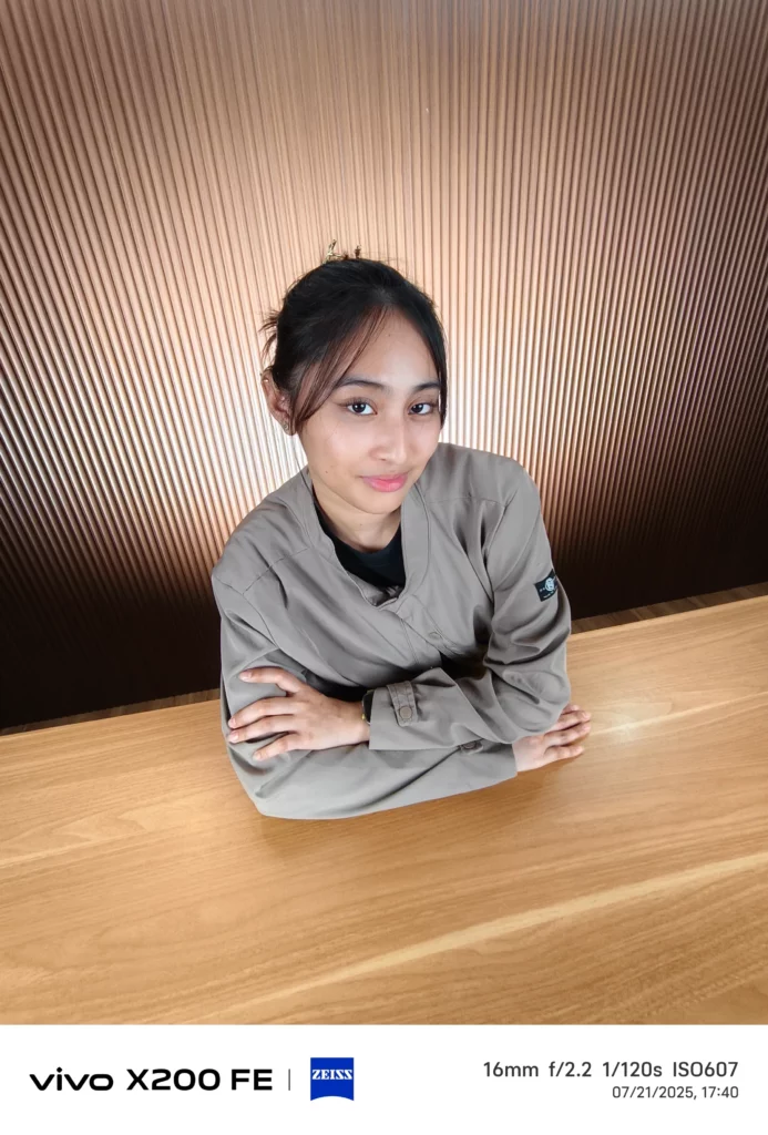 Young woman in a jacket leaning on a wooden table, against a striped wall.