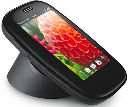 A black Palm Pre smartphone sits on a matching black wireless charging dock, with a colorful floral wallpaper on its screen.