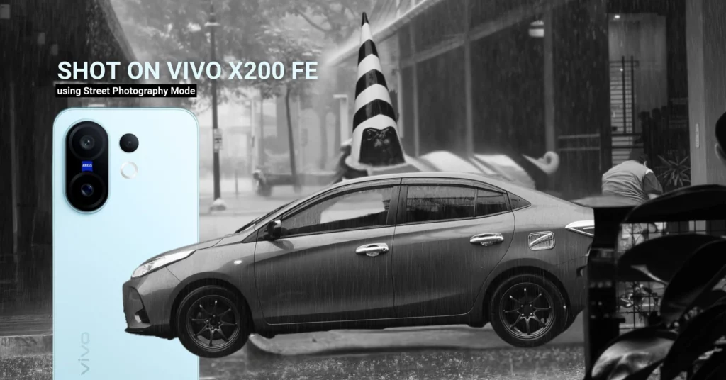 A promotional graphic for the vivo X200 FE. The phone is shown in the left foreground in a light blue color. A black and white photo of a silver car on a rainy street is in the background, with a black and white striped cone visible. The text "SHOT ON VIVO X200 FE" and "using Street Photography Mode" is overlaid on the image.