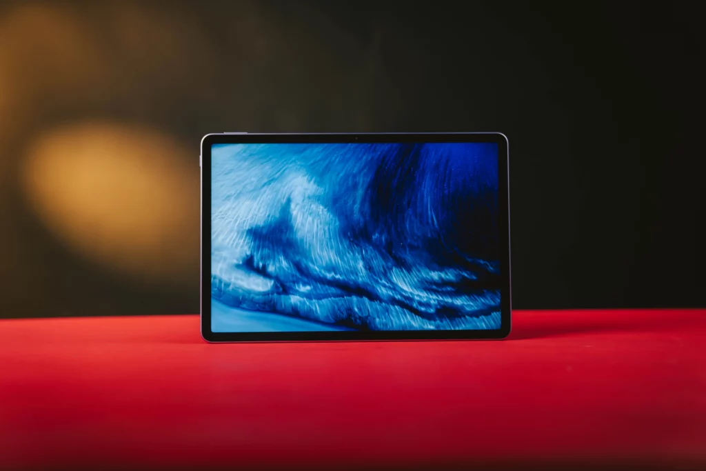 The HUAWEI MatePad 11.5 tablet standing upright on a red surface, with the screen displaying a vibrant, flowing blue and white abstract wallpaper.