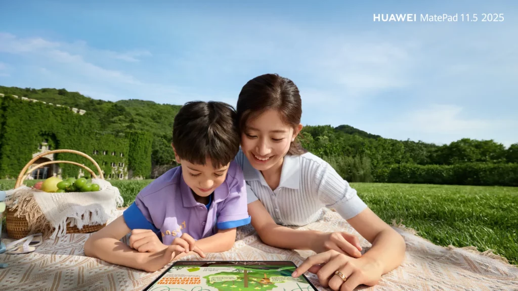 A young woman and a child lie on a picnic blanket in a grassy park, sharing a Huawei MatePad 11.5 tablet to play or learn from its screen.