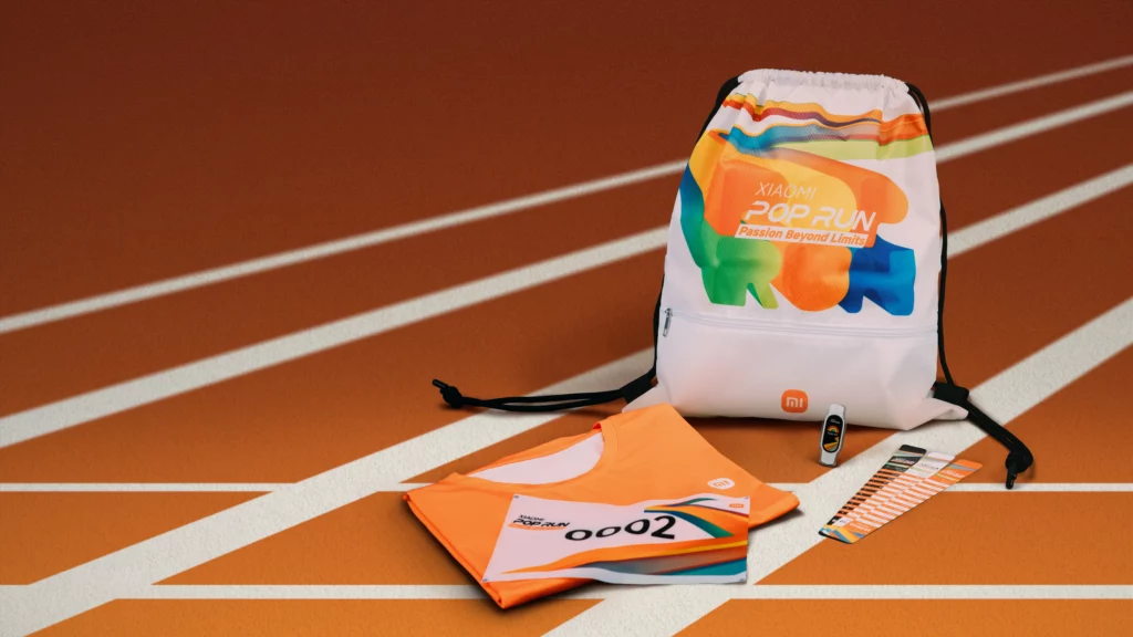 A flat lay of promotional items for the Xiaomi Pop Run. The items are a white drawstring bag with colorful, abstract graphics and the words 'Xiaomi Pop Run,' a folded orange running t-shirt with a race number '0002,' and a race bib with a small timer device.