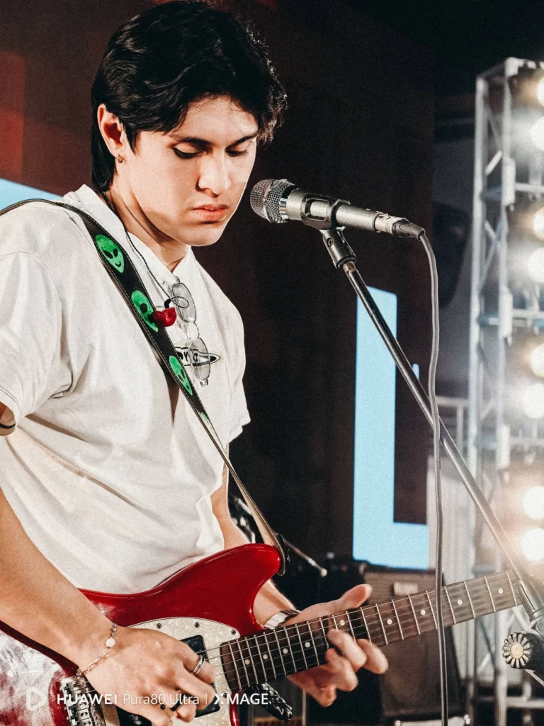 A male musician playing a red electric guitar on stage, taken with the Huawei Pura80 Ultra.