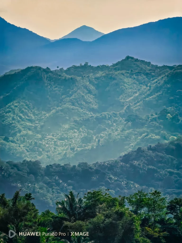A vibrant landscape photo of green and blue mountains under a bright sky, taken with the Huawei Pura80 Pro.