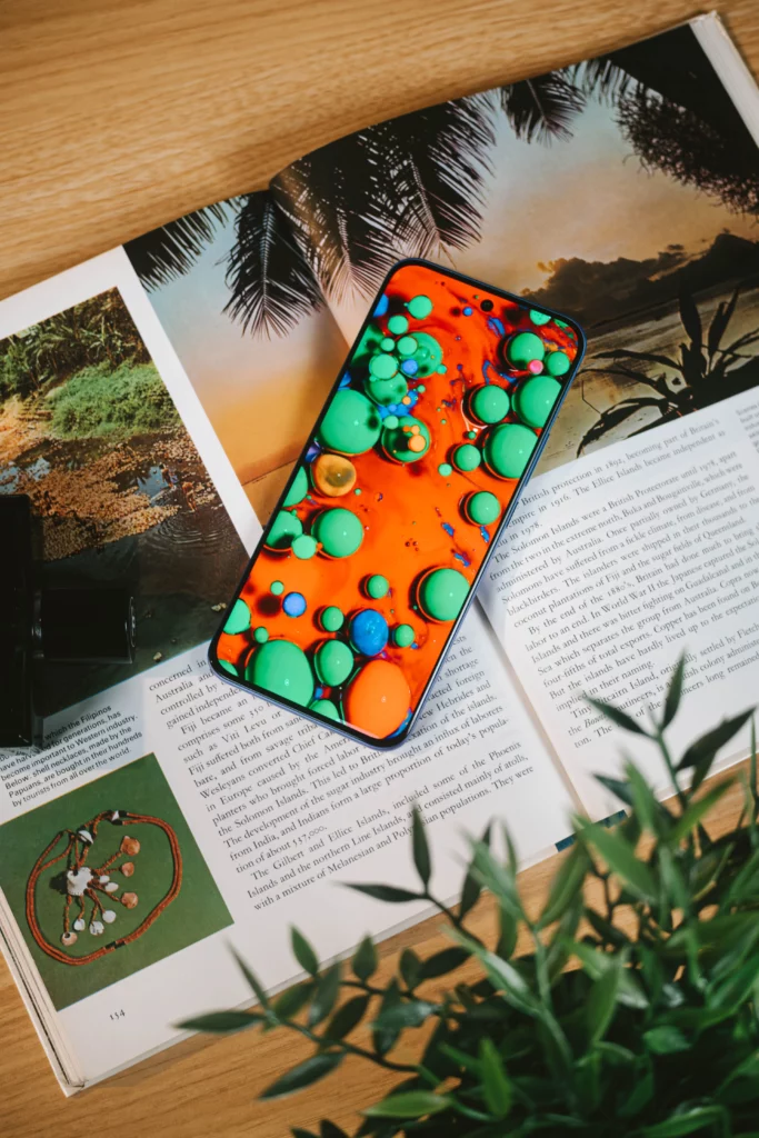 The Infinix HOT 60 Pro+ smartphone displaying a vibrant, colorful abstract wallpaper, resting on an open book about Fiji.