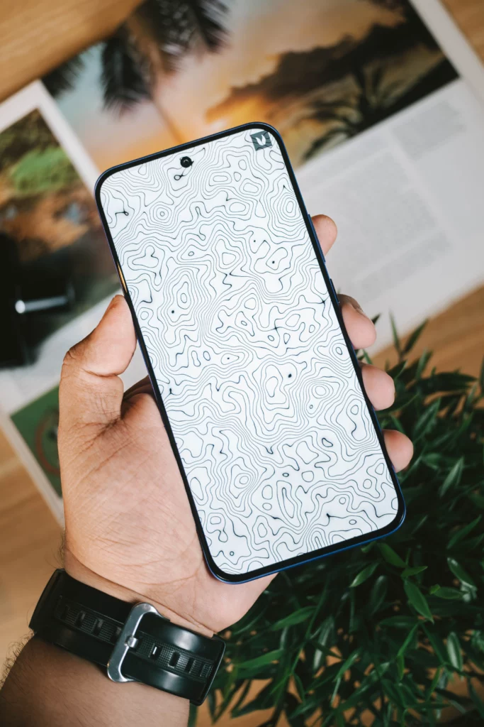 A hand holding the Infinix HOT 60 Pro+ smartphone, which is displaying a black and white topographic map wallpaper.