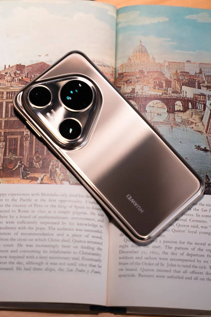 A silver HUAWEI Pura80 Ultra smartphone is placed open on a book, with its unique camera module visible on the top and the "HUAWEI" logo on its back. The book features text and an illustration of a historical city.