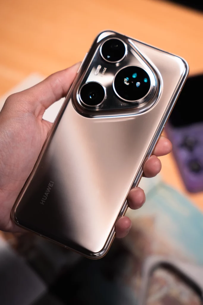 A hand holds a silver HUAWEI Pura80 Ultra smartphone, displaying its sleek, reflective back and the uniquely designed camera array with three lenses and the "HUAWEI" logo near the bottom.