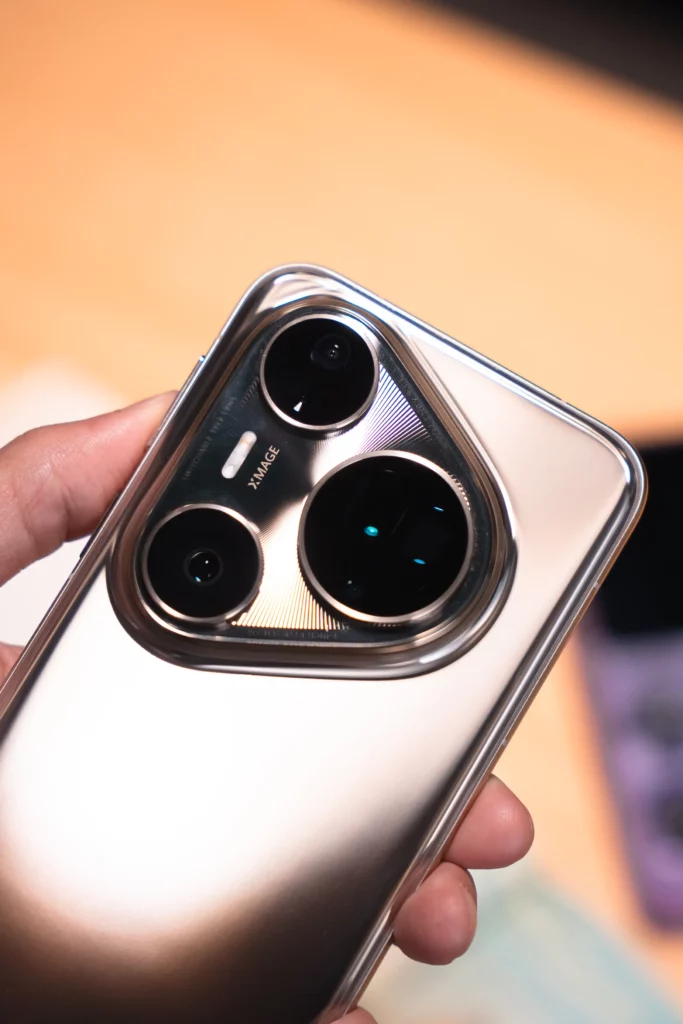 A close-up of the back of a silver HUAWEI Pura80 Ultra smartphone, held in a hand. The prominent, unique camera module with three large lenses and the "XMAGE" branding is visible.