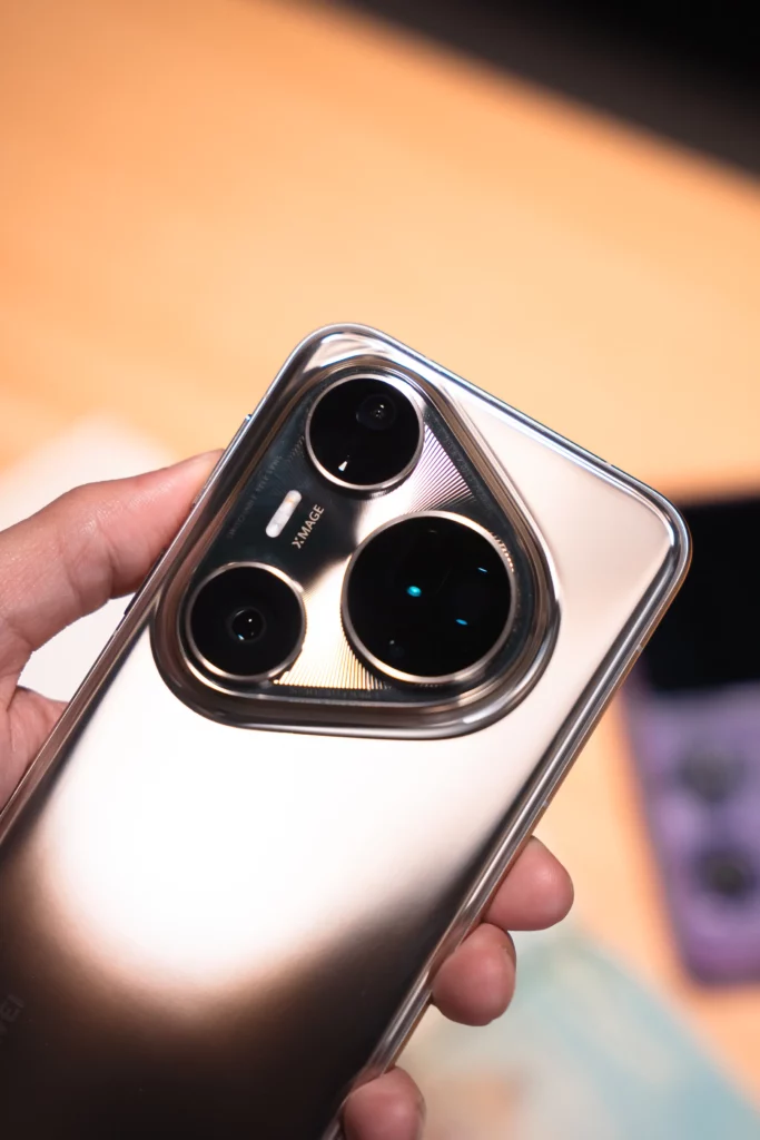 A hand holds a silver HUAWEI Pura80 Ultra smartphone, showcasing the device's back with its large, distinctive camera module containing three lenses and the "XMAGE" logo.