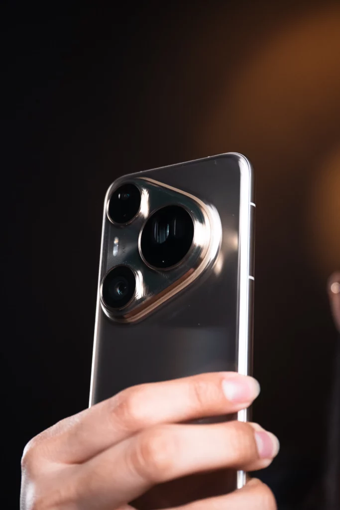 A close-up of a hand holding a silver HUAWEI Pura80 Ultra smartphone, showcasing the side profile of the device and its large, distinctive camera module with three lenses.