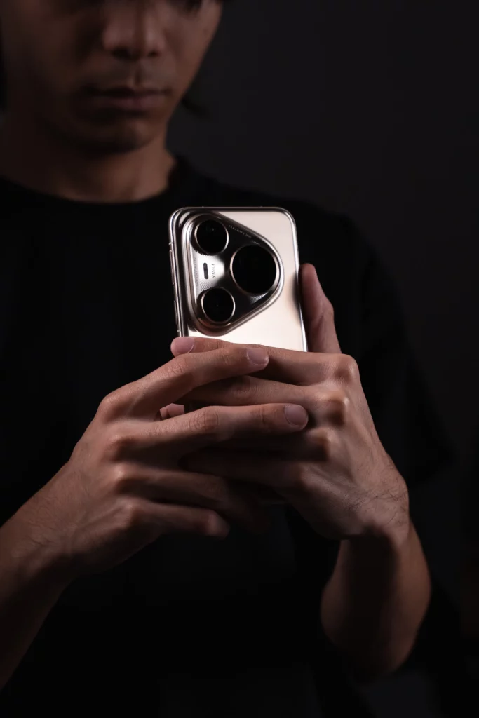 A person's hands hold a silver HUAWEI Pura80 Ultra smartphone, with the camera module prominently displayed. The background shows the upper body of the person in shadow.