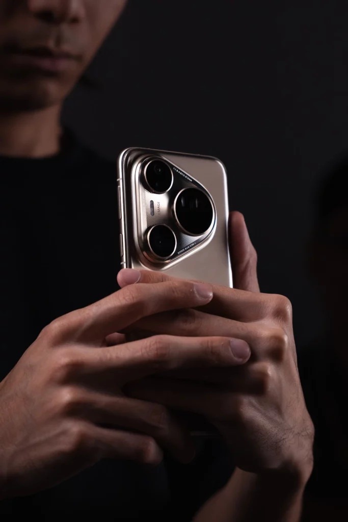 A person with a blurred face in the background holds a silver HUAWEI Pura80 Ultra smartphone with both hands, showcasing its prominent three-lens camera module. The phone is lit from the front, creating a subtle shine.