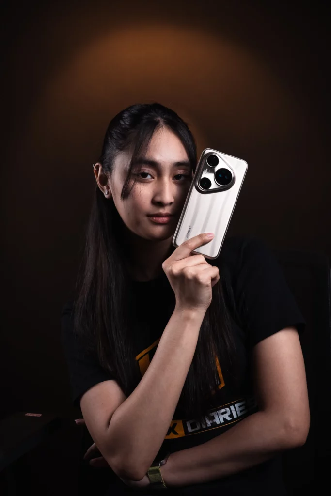 A young woman with long dark hair, wearing a black t-shirt, holds up a silver HUAWEI Pura80 Ultra smartphone with the camera module facing forward, looking directly at the viewer.