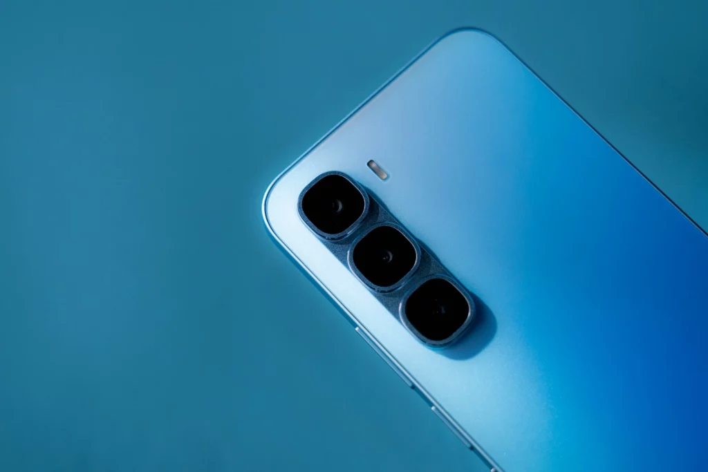 A detailed close-up of the triple-camera module on the back of a light blue Infinix smartphone. The three camera lenses are arranged vertically, and the phone's surface has a subtle gradient effect.