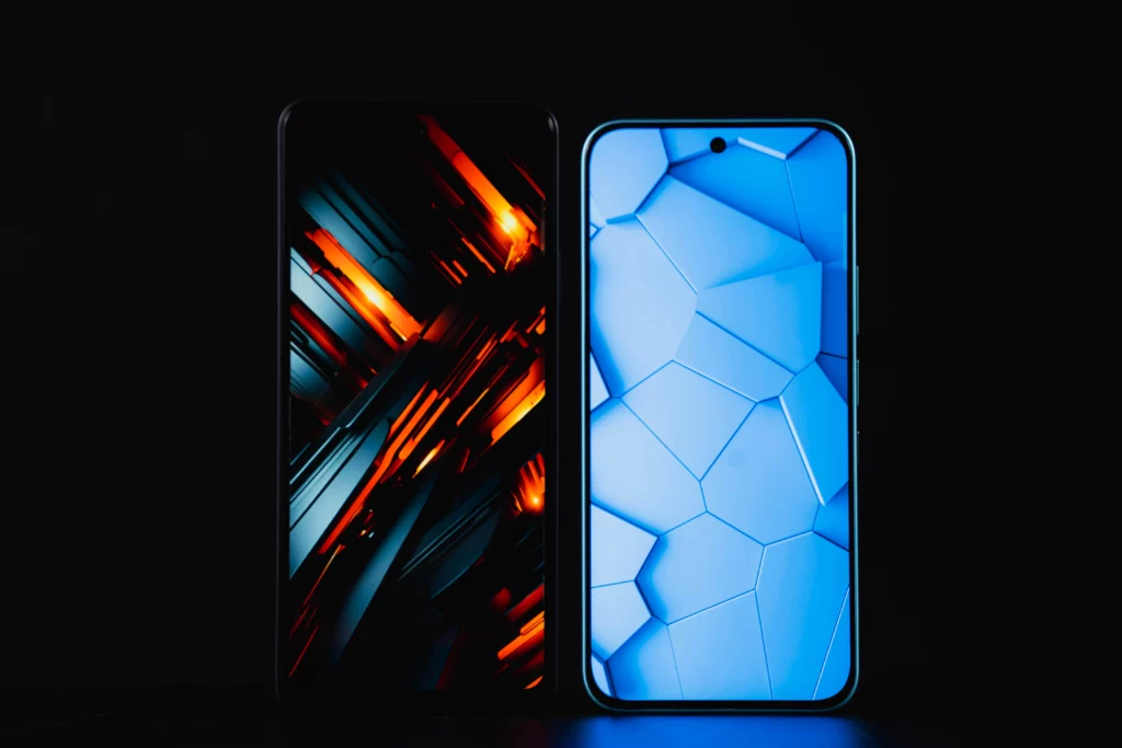 Two smartphones are shown side-by-side from the front, against a black background. The phone on the left displays a fiery, dark orange and black geometric wallpaper. The phone on the right has a light blue, hexagonal pattern wallpaper. Both phones have a punch-hole camera cutout at the top of the screen.