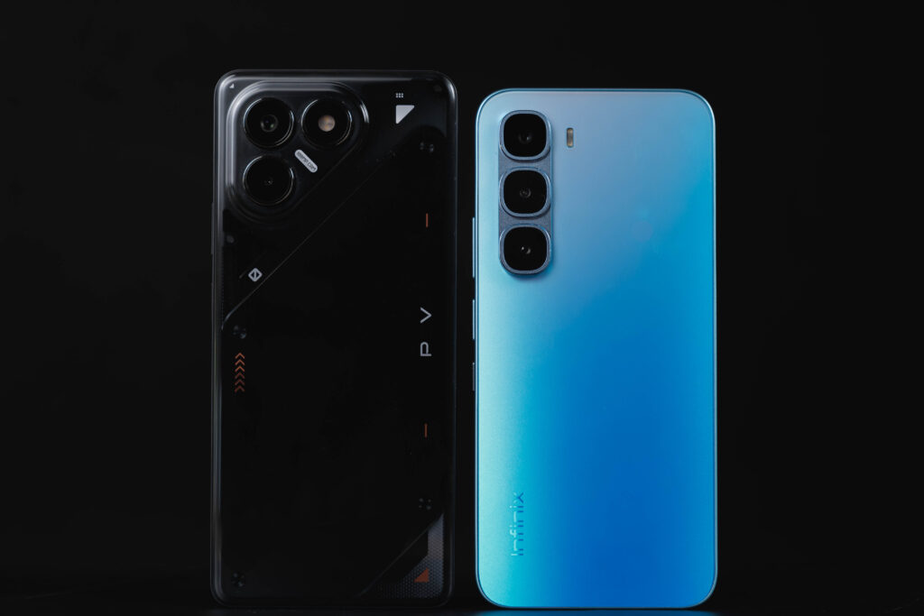 A studio shot of two smartphones against a solid black background. The black phone on the left has a futuristic, industrial-style back panel with a large circular camera island. The blue phone on the right has a simpler, clean design with a vertical triple-camera array and the Infinix logo at the bottom.