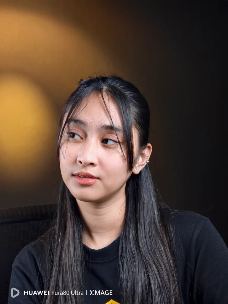 A portrait of a young woman with long dark hair, wearing a black t-shirt, looking off to the side with a gentle expression. The HUAWEI Pura80 Ultra | XMAGE watermark is in the bottom left corner.