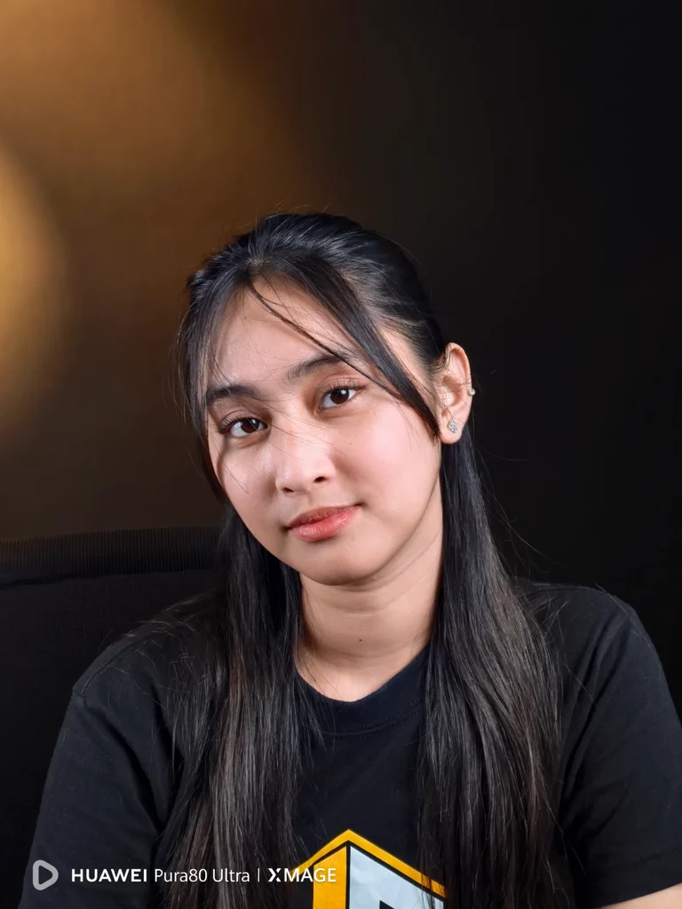 A portrait of a young woman with long dark hair, wearing a black t-shirt, looking directly at the camera with a soft expression. The HUAWEI Pura80 Ultra | XMAGE watermark is in the bottom left corner.