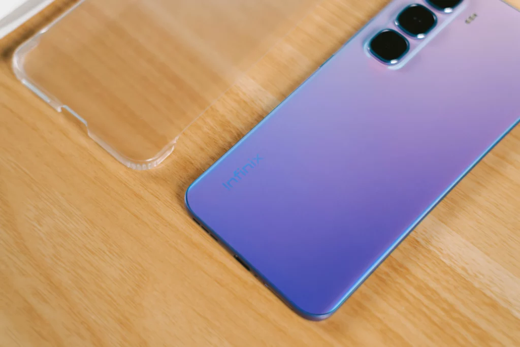 Close-up of the Infinix logo on the bottom rear of the purple HOT 60 Pro+, next to a clear phone case.