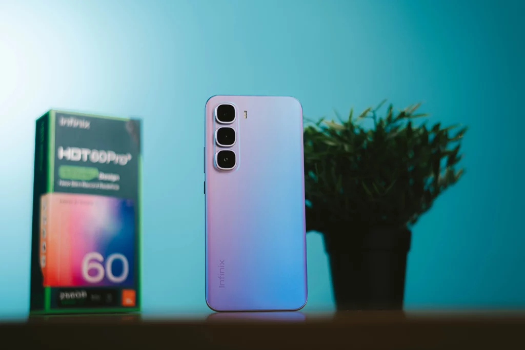 Infinix HOT 60 Pro+ in purple, standing upright next to its retail box and a green potted plant.