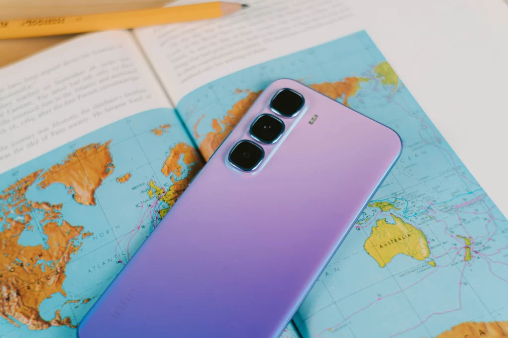 Purple Infinix HOT 60 Pro+ with triple cameras lying on an open atlas, featuring Australia and a pencil.