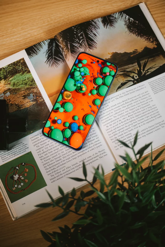  Infinix HOT 60 Pro+ displaying a vibrant, bubbly wallpaper, lying on an open magazine.