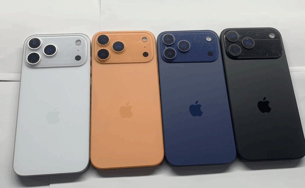 Four iPhone 17 Pros in different colors—white, orange, blue, and black—are placed side by side with their backs facing up, showing the Apple logo and camera modules.