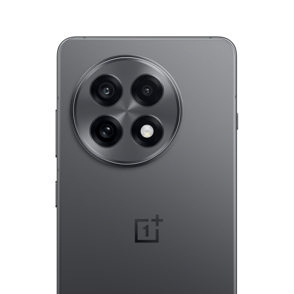 A high-resolution image of the back of a dark gray smartphone, likely the OnePlus 13R. The phone has a large, circular camera module with a brushed metal finish, containing four lenses and an LED flash. The OnePlus logo is centered below the camera module. A caption below the image reads "OnePlus 13R via, OnePlus".