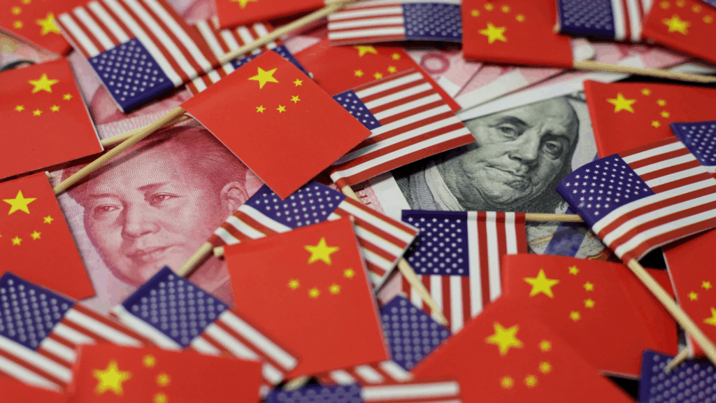 A collage of miniature American and Chinese flags scattered over Chinese yuan and US dollar banknotes, symbolizing the US-China trade war.