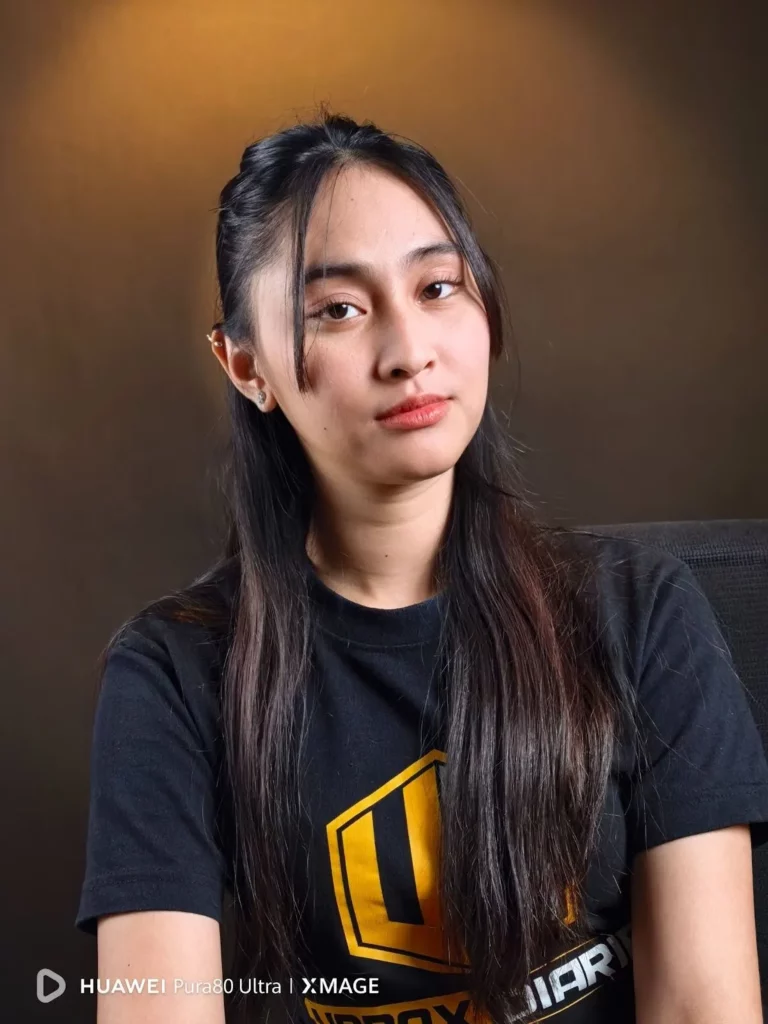 A portrait of a young woman with long dark hair, wearing a black t-shirt with a yellow logo, looking directly at the camera with a serious expression. The HUAWEI Pura80 Ultra | XMAGE watermark is in the bottom left corner.