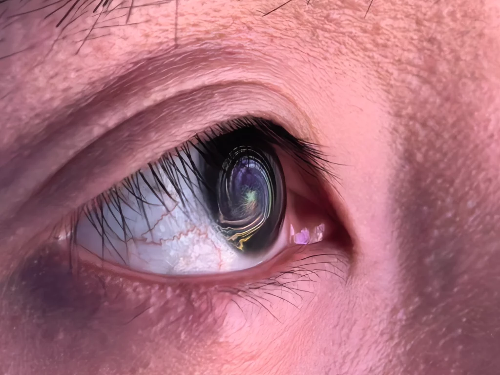 An extreme close-up of a human eye. The pupil reflects a swirling, abstract pattern of vibrant colors, with the iris and lashes in sharp detail.