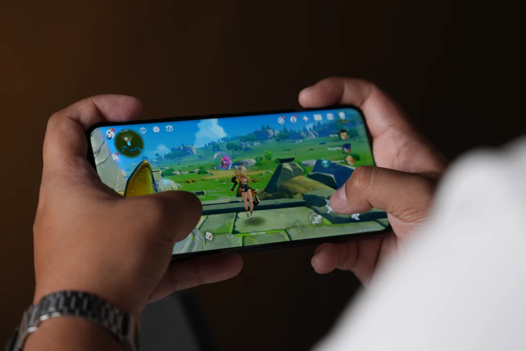A shot of a person holding the Vivo V60 smartphone horizontally while actively playing Genshin Impact, with their fingers on the screen.
