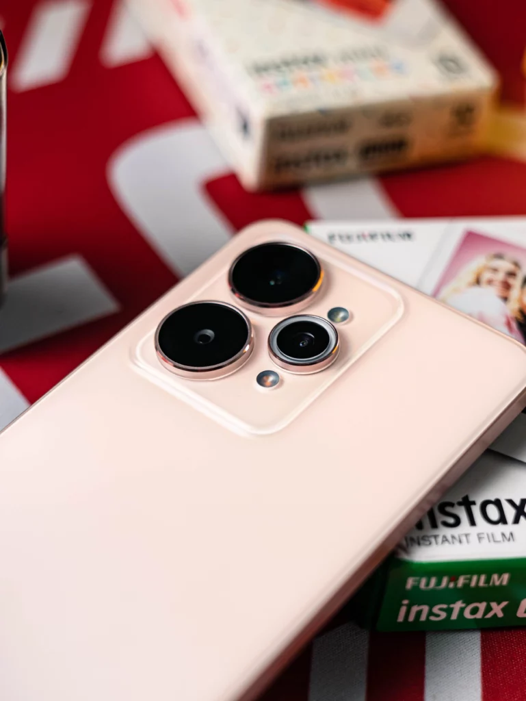 A close-up shot of the realme 15 5G's back, focusing on the camera module and flash. The phone is placed on a red and white surface next to a pack of Instax film. This shot is nearly identical to 15.jpg but with a slightly different depth of field.