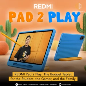 An advertisement for the Redmi Pad 2 Play. The image features a blue tablet in a protective case with a yellow kickstand. The screen displays a person in a black T-shirt with the Unbox Diaries logo on it. To the right, a second blue tablet is shown from the side and back, also propped up. The background is an orange and green landscape with cartoon-style cacti. Large text at the top reads "REDMI PAD 2 PLAY," with "REDMI" in white and "PAD 2 PLAY" in large orange and blue letters. A yellow banner at the bottom describes the product as "The Budget Tablet for the Student, the Gamer, and the Family." The Unbox Diaries logo is in the top right corner.