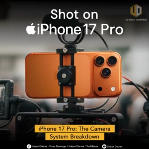 An orange-colored iPhone 17 Pro is mounted on a professional camera rig, with a microphone and other accessories attached. The phone's three large camera lenses are clearly visible on the back. Large white text at the top of the image reads, "Shot on iPhone 17 Pro." A yellow banner at the bottom says, "iPhone 17 Pro: The Camera System Breakdown." The image is focused on the phone, while the background of what appears to be a film set is blurred.