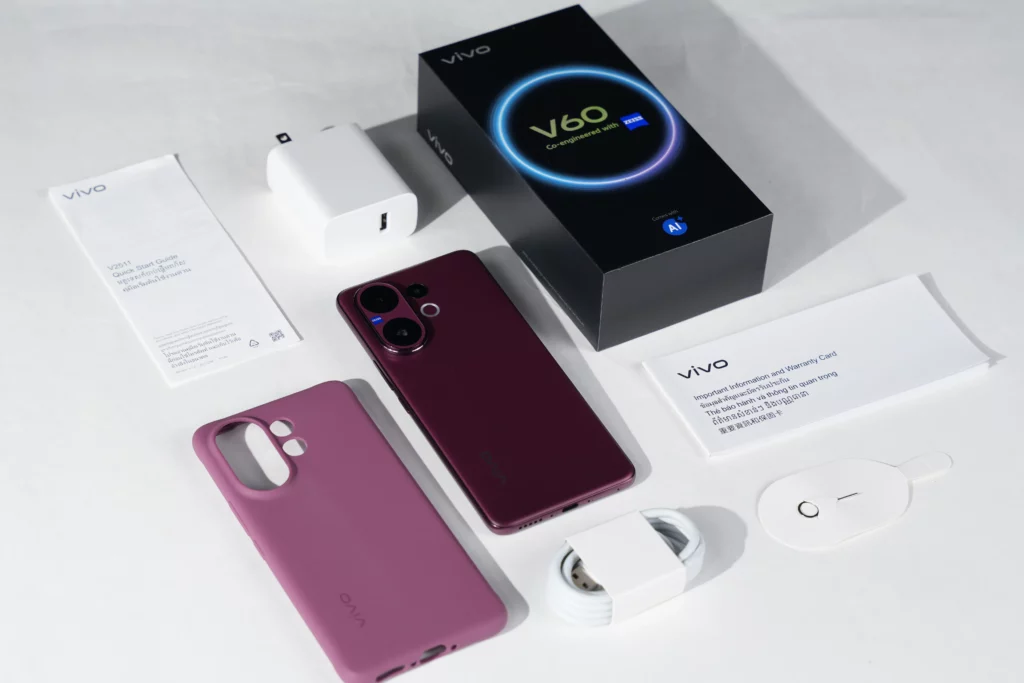 The full unboxing contents of the Vivo V60 laid out on a white surface, including the smartphone, its retail box, a charger, USB cable, a purple protective case, and various documentation.