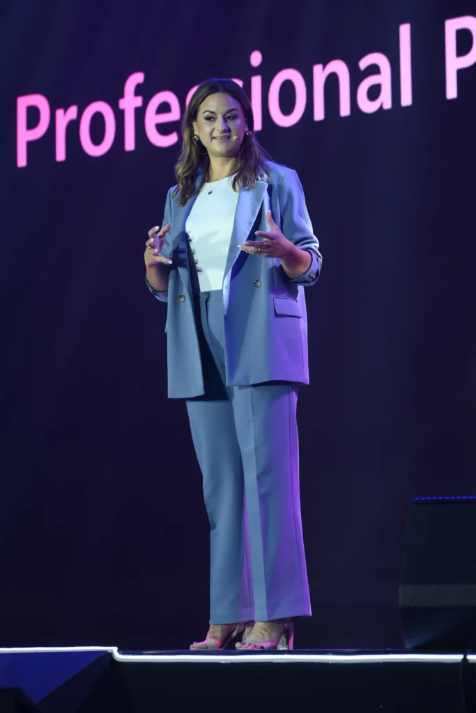 Franziska Hoffmann, Brand Partnerships Manager for ZEISS Photonics & Optics, is speaking on a stage. She is wearing a light blue suit and a white shirt. The background is dark with pink text that says "Professional P..."