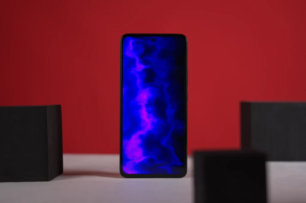 A black smartphone with a vibrant blue and purple abstract or cosmic wallpaper displayed on its screen, set against a red background with black blocks.