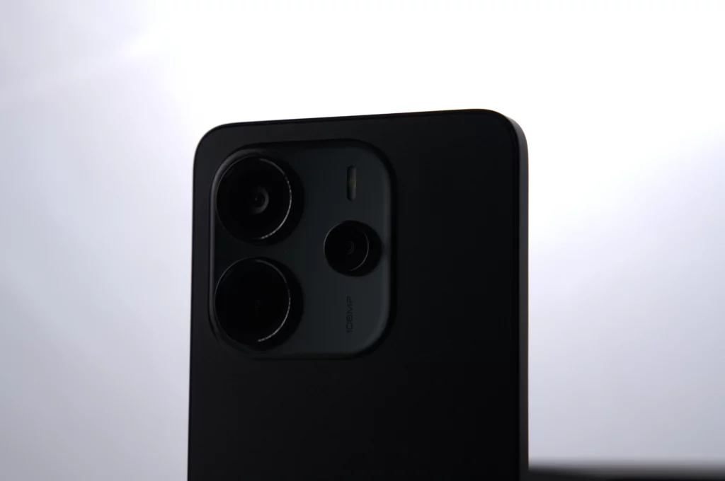 A close-up shot of the camera lenses and 108MP AI camera text on the back of a black Redmi Note 14 smartphone.