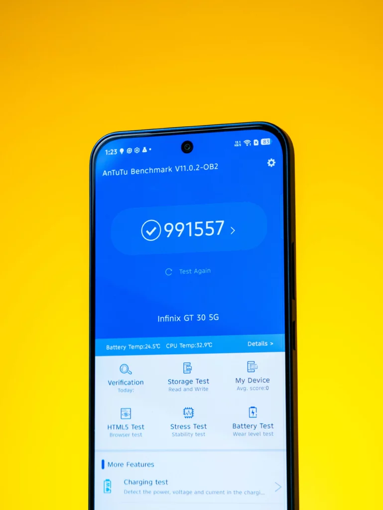 A vertical shot of the smartphone screen displaying the results of the AnTuTu Benchmark V11.0.2. The large score of 991557 is prominently visible, along with the device name "Infinix GT 30 5G" and various system tests. The phone is set against a bright yellow background.