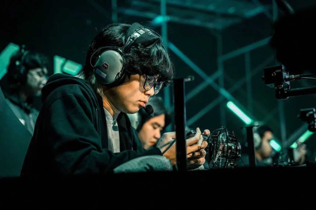 A close-up of an MPL player in a headset and glasses, focused on their phone during a competitive match.