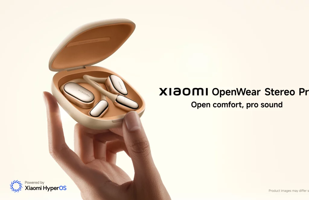 A hand gently holds the open charging case for the Xiaomi Openwear Stereo Pro earbuds. The tan-colored case holds two beige, open-ear earbuds, one for each ear. The text "Xiaomi OpenWear Stereo Pro" and "Open comfort, pro sound" is visible.