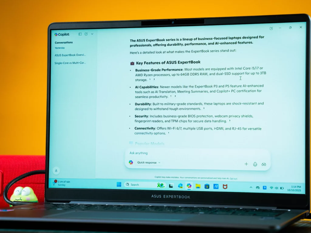 The laptop screen displays the Microsoft Copilot interface, showing a summary of the "Key Features of ASUS ExpertBook," which includes details on Business-Grade Performance, AI Capabilities, Durability, Security, and Connectivity.