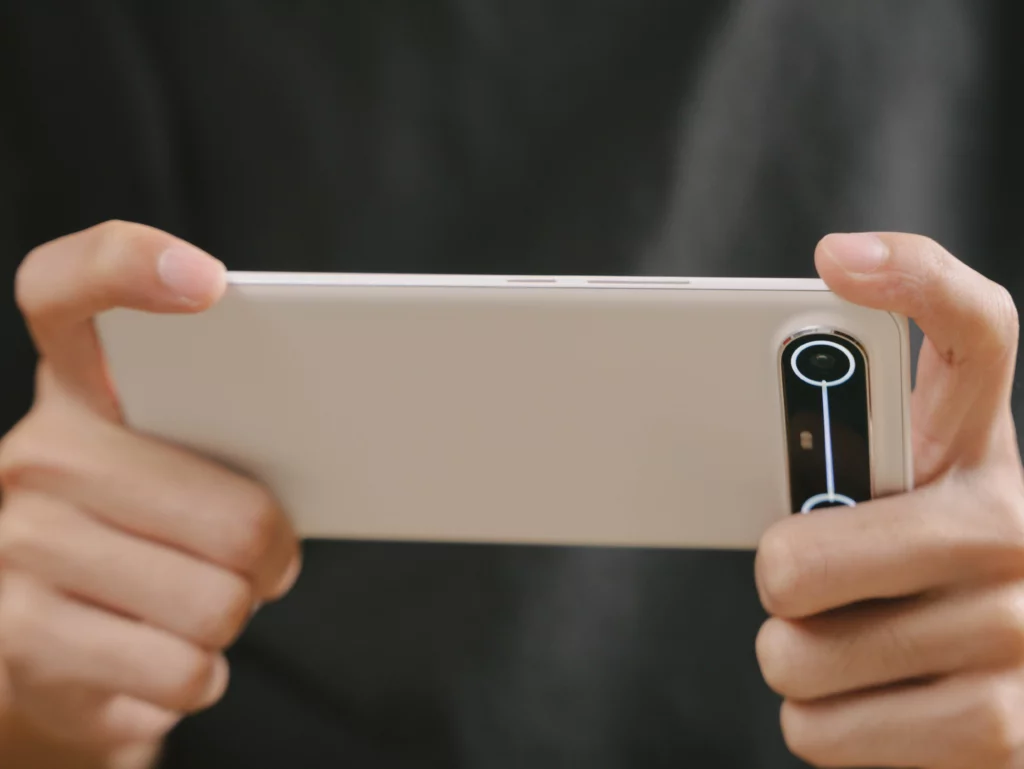 Hands holding the white TECNO SPARK Slim horizontally, likely for gaming or watching a video, showing the side profile and the camera module.