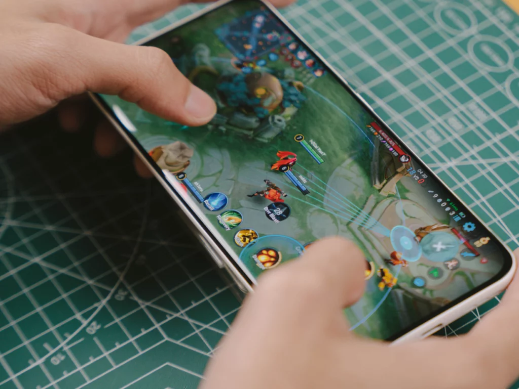 Hands holding the TECNO SPARK Slim horizontally while playing a mobile MOBA game, showcasing the display quality and thin bezels.